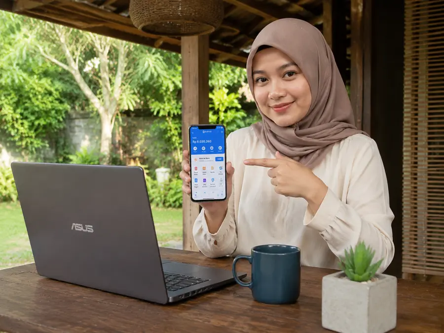 Perempuan berhijab bekerja online dengan laptop dari ruang terbuka di rumah